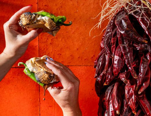 Two hands holding S'mores against a red background with dried Hatch Peppers on the side.