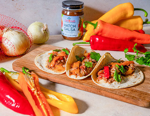 Long Sweet Pepper and Beef Fajitas made with marinated flank steak, colorful sweet peppers, Hatch onions, and zesty Hatch salsa on a wooden cutting board.