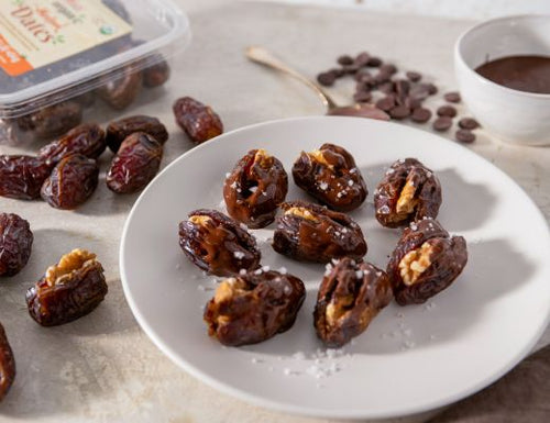 Chocolate-dipped walnut stuffed Medjool dates topped with flaky sea salt on a serving plate.