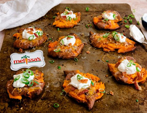 Loaded smashed baby yams topped with melted cheddar cheese, sour cream, crispy bacon, and green onions on a baking sheet.