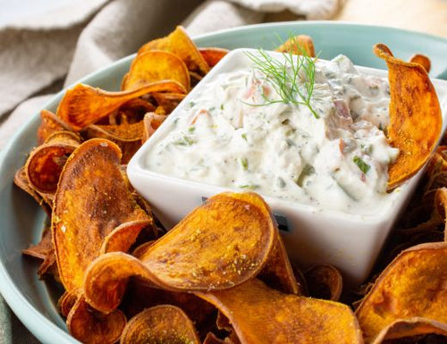 Crispy spiced garnet yam chips served with creamy cucumber herb dip in a white bowl.
