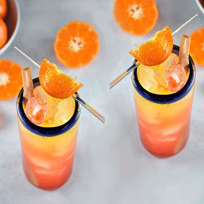 Tangerine Tequila Sunrise in blue rimmed water glasses on a gray surface