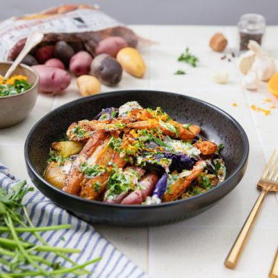 Golden crispy smashed fingerling potatoes with herbs, toasted garlic, and citrus zest in a black bowl with fresh ingredients in the background