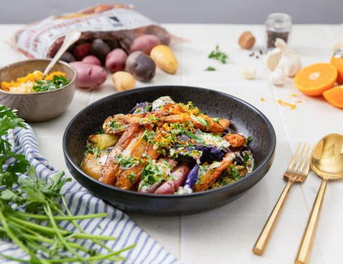 Golden crispy smashed fingerling potatoes with herbs, toasted garlic, and citrus zest in a black bowl with fresh ingredients in the background