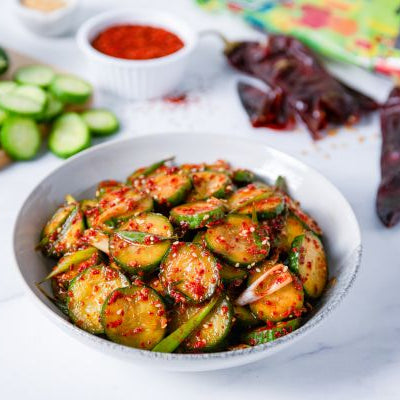 Korean-style cucumber banchan with sliced cucumbers in a red Hatch pepper dressing, garnished with green onions