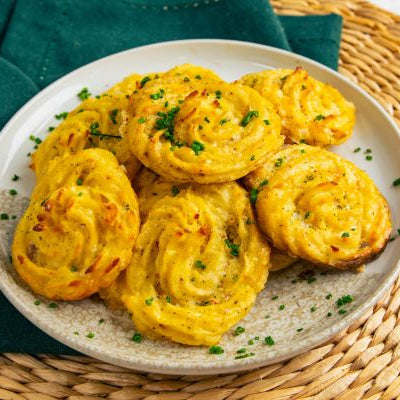 Garlic Parmesan Duchess potatoes piped into swirls, baked until golden brown with crispy edges, and garnished with fresh herbs on a serving plate