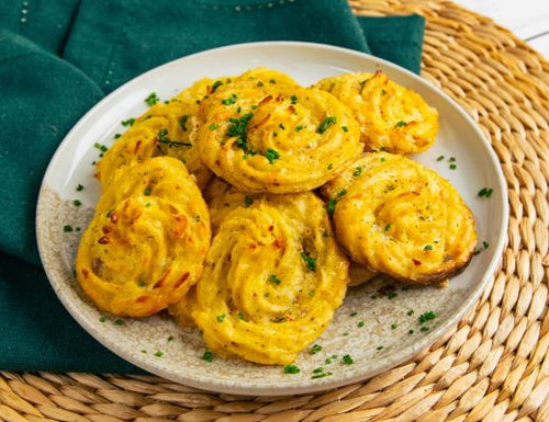 Garlic Parmesan Duchess potatoes piped into swirls, baked until golden brown with crispy edges, and garnished with fresh herbs on a serving plate