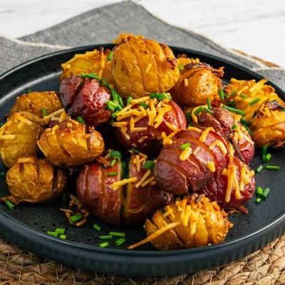 Hot honey buttered Hasselback Dutch potatoes roasted until golden and crispy, topped with melted cheese and fresh chives on a serving plate