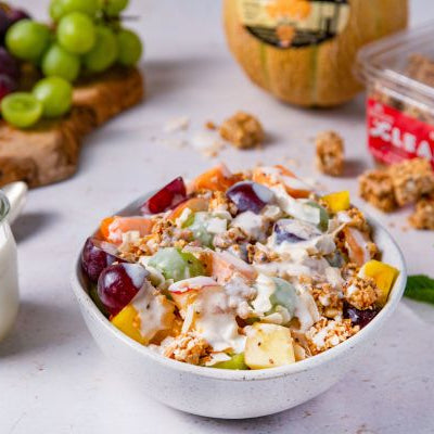 Bowl of fruit salad with granola on a table with grapes and a jar of yogurt (Bionico)