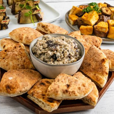 Creamy lemony eggplant yogurt dip with pita wedges and roasted appetizers in the background