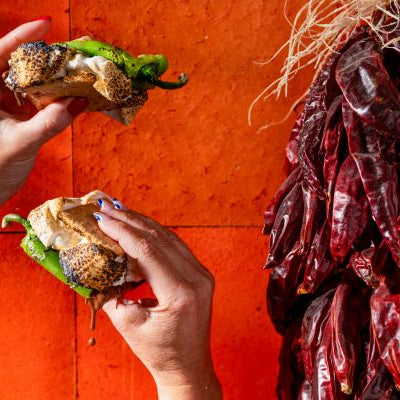 Two hands holding S'mores against a red background with dried Hatch Peppers on the side.