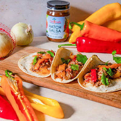 Long Sweet Pepper and Beef Fajitas made with marinated flank steak, colorful sweet peppers, Hatch onions, and zesty Hatch salsa on a wooden cutting board.