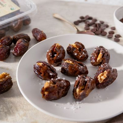Chocolate-dipped walnut stuffed Medjool dates topped with flaky sea salt on a serving plate.