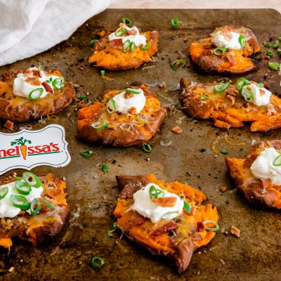 Loaded smashed baby yams topped with melted cheddar cheese, sour cream, crispy bacon, and green onions on a baking sheet.