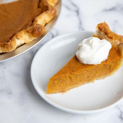 Slice of homemade sweet potato pie with a creamy spiced filling and whipped cream on top, served on a white plate.