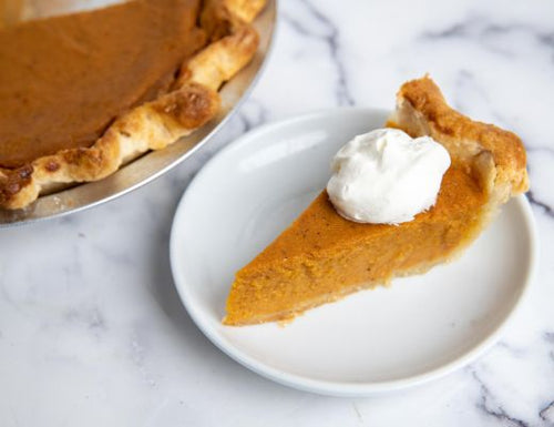 Slice of homemade sweet potato pie with a creamy spiced filling and whipped cream on top, served on a white plate.