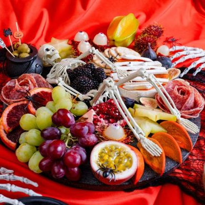 Freaky Fruit Boocuterie Halloween grazing board with fresh fruit, berries, grapes, citrus, passion fruit, and spooky skeleton decorations