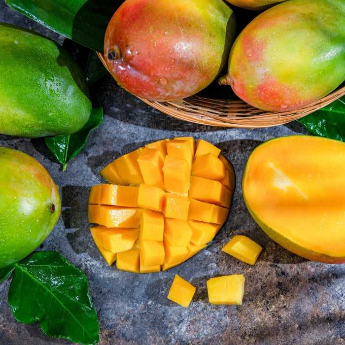 whole and sliced green and green + red mangos on a gray background.