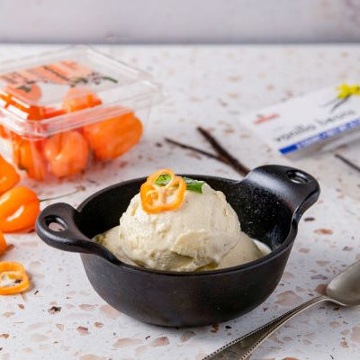 Habanero-Vanilla Ice cream in a black bowl with chili peppers on a speckled countertop