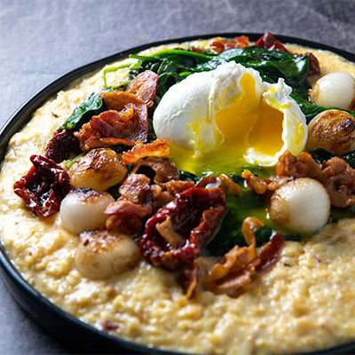 Image of Poached Eggs over Polenta with Crispy Pancetta, Sun Dried Tomatoes, Wilted Spinach and Pearl Onions