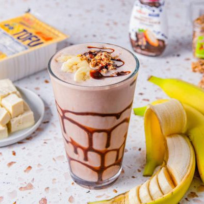 Chocolate milkshake with banana slices and tofu squares on a table.