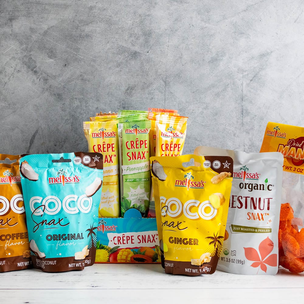 A variety of clean snax, coco snax, crepe snax, chestnut snax, and dried fruit snax on a white wooden table.