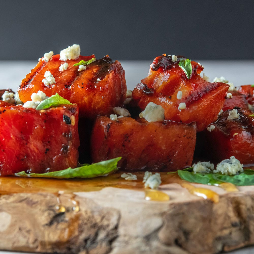 Diced watermelon with basil and blue cheese on a wooden board with a dark background