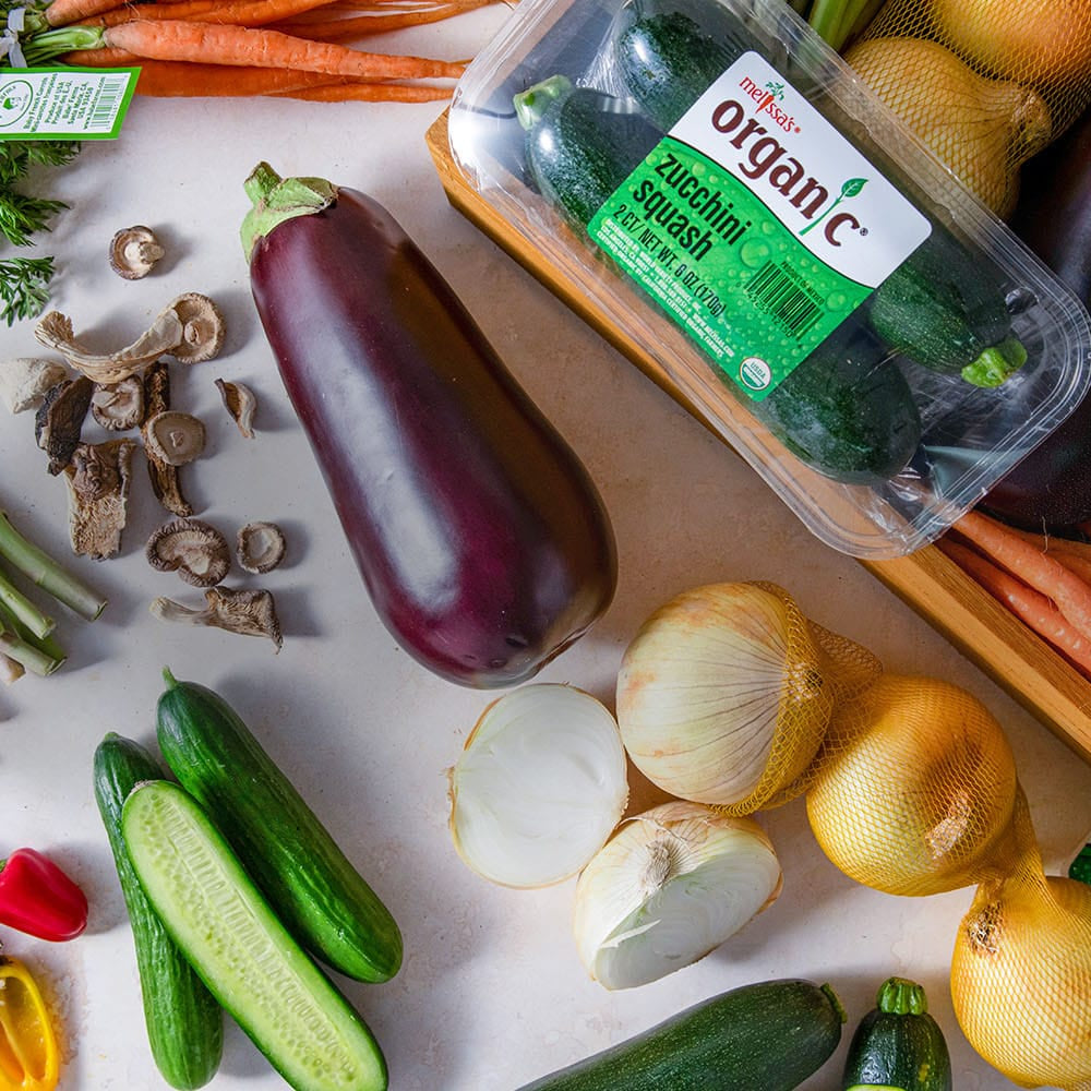 Assorted fresh vegetables including carrots, cucumbers, eggplant, dried mushrooms, onions, zucchini, and veggies sweet peppers on a white surface.