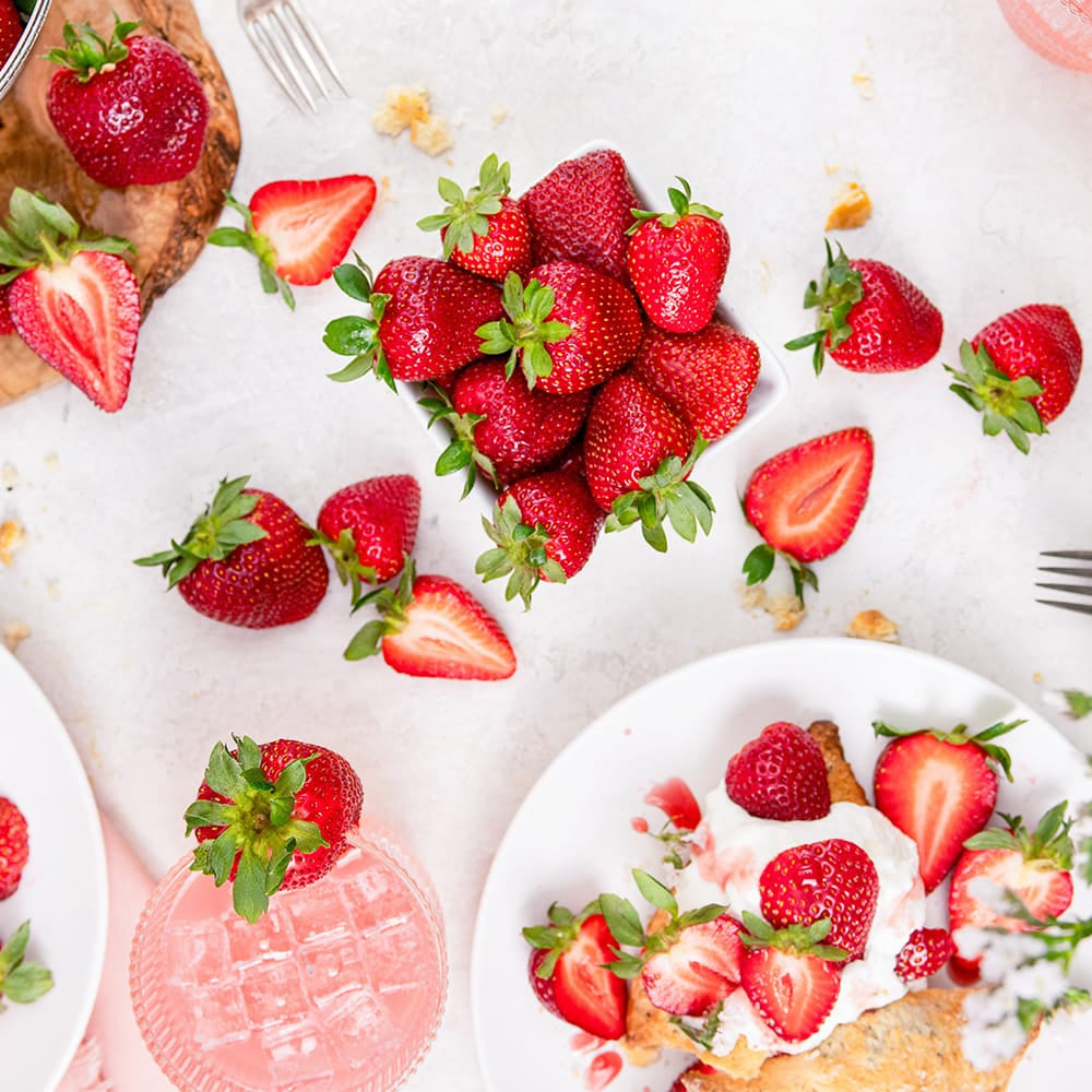 Table setting with strawberries on plates and a bowl, surrounded by flowers.