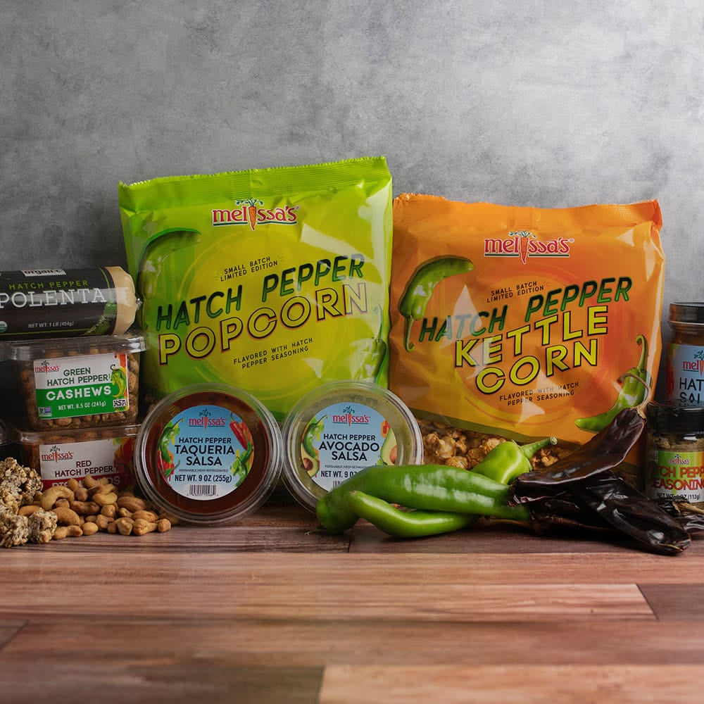Assorted Hatch Pepper products including popcorn, peppers, salsas, polenta, snacks, and sauces on a wooden table with a gray background.