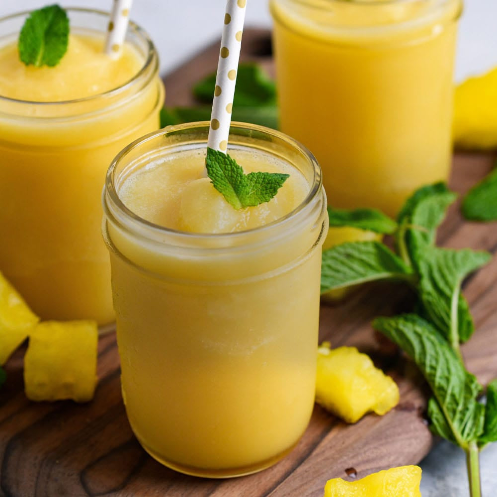 Three glasses of yellow melon smoothie with mint leaves on a wooden board.