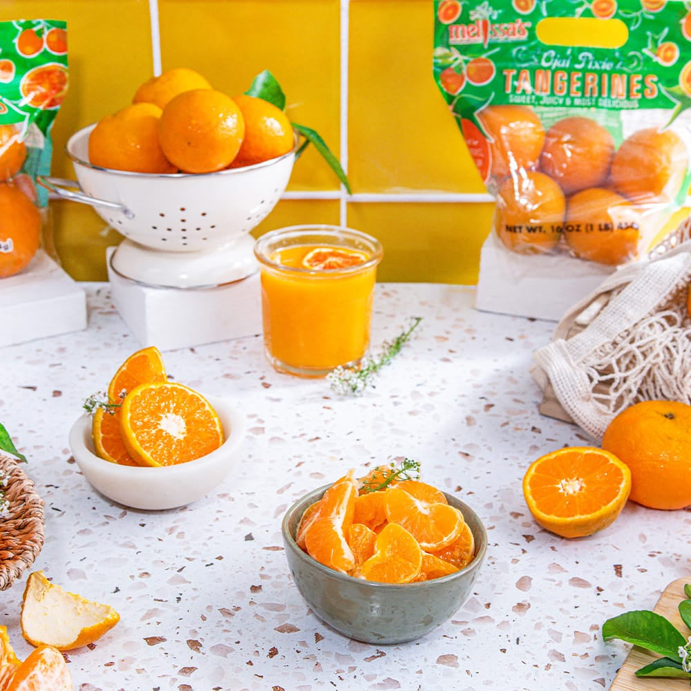 Tangerines and juice on a table with Melissa's packaging in the background.