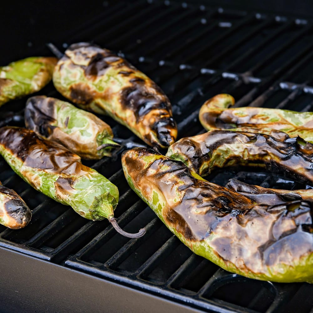 Charred green peppers grilling on a black metal barbecue grill grate.