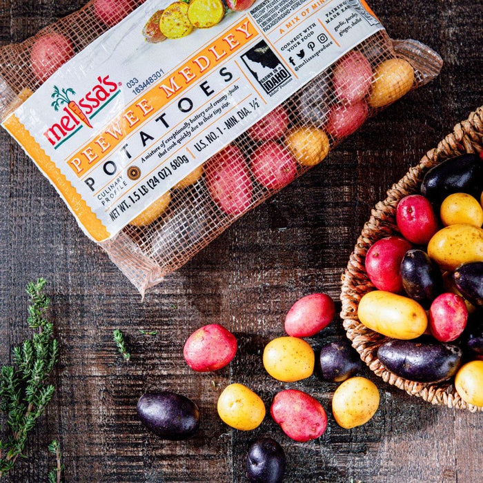 Peewee Potato Medley , red, purple and yellow baby potatoes in a see through sack on a wooden surface. There are also those potatoes in a basket next to the sack.