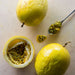Yellow Passion Fruit and one of them halved with a spoon that has the pulp in it on a white surface..